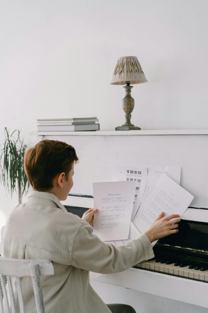 A young boy organizes sheet music while sitting at a piano, indicating his passion for music.
